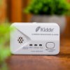 kidde 2030 dcr carbon monoxide alarm placed on a wooden surface with a blurred plant in the background