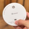 kidde 2030 dsr optical smoke alarm held in hand with finger pressing the test button shown without plant