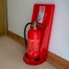 Ultrafire economy fire extinguisher stand single red holding a red fire extinguisher placed against a white wall on a carpeted floor
